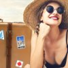 Donna con cappello sulla spiaggia accanto a una valigia.