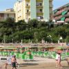 Una spiaggia con ombrelloni verdi e arancioni e un hotel sullo sfondo.