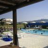 Piscina all'aperto con lettini e ombrelloni, persone che nuotano e panorama collinare sullo sfondo.