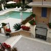 Piscina con lettini e ombrelloni in un cortile ben curato, adornato da fiori rossi.