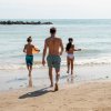 Persone camminano verso il mare su una spiaggia sabbiosa.